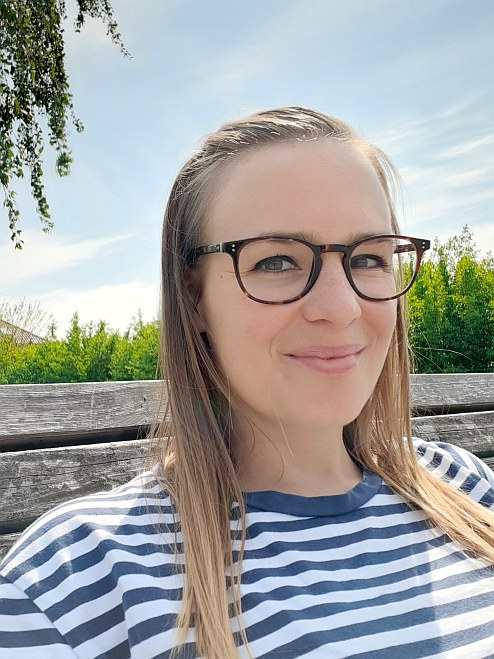 Ulla Scharfenberg mit offenen Haaren und Brille auf einer Parkbank im Grünen